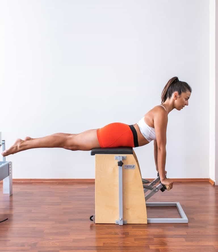A woman performs a Pilates exercise on a Wunda chair, showcasing strength and balance.