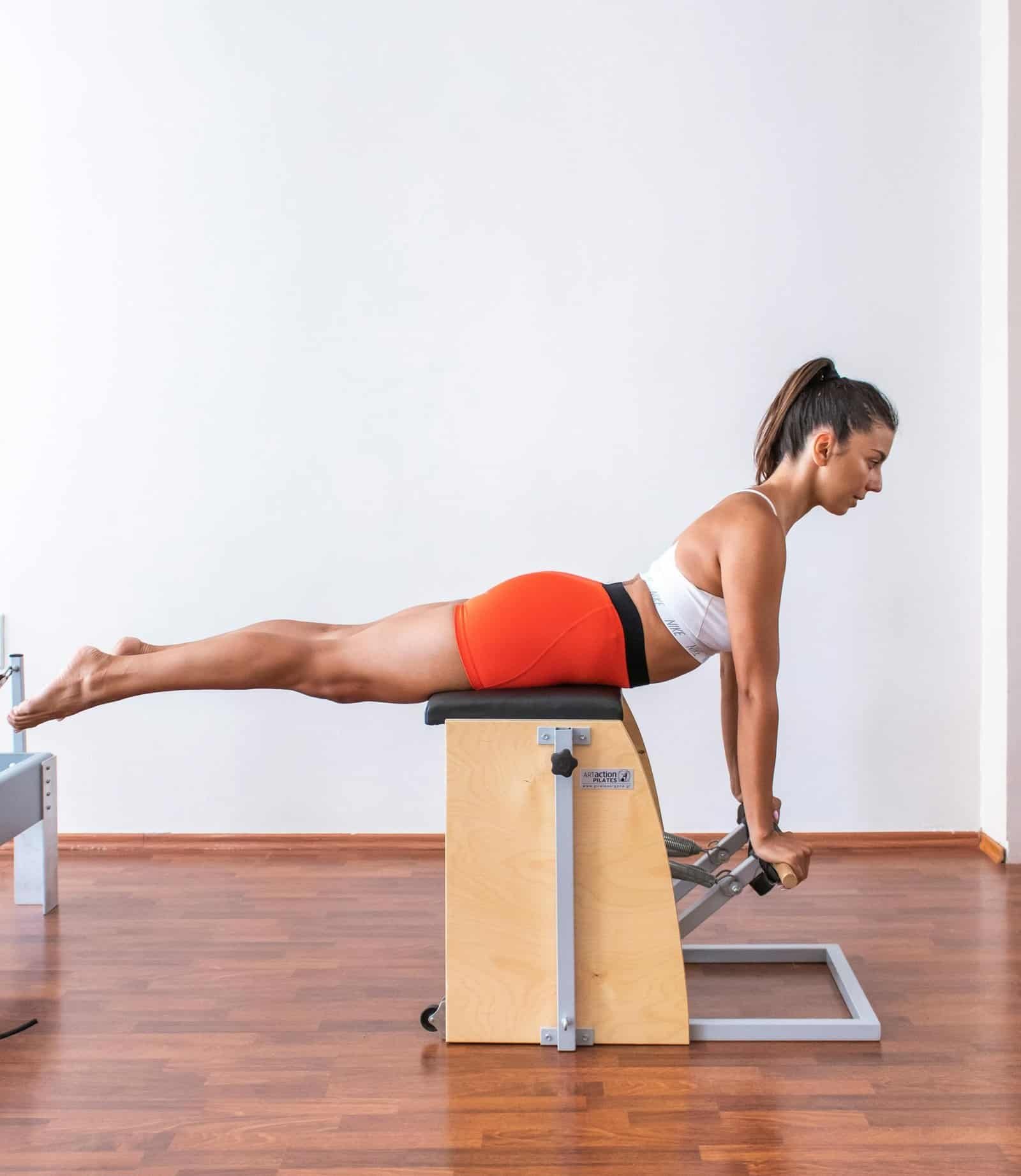A woman performs a Pilates exercise on a Wunda chair, showcasing strength and balance.