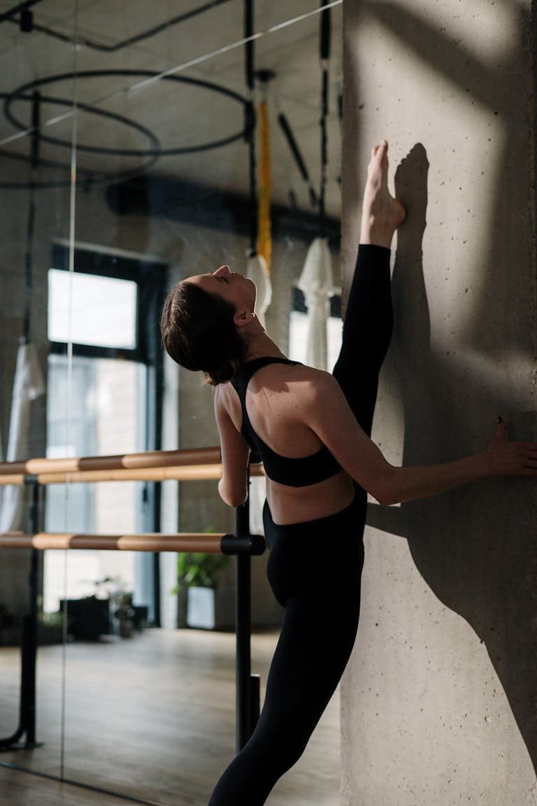 A woman stretches against a concrete wall in a bright yoga studio, demonstrating flexibility.