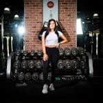 Confident young woman standing in a gym, surrounded by dumbbells, exuding fitness motivation.