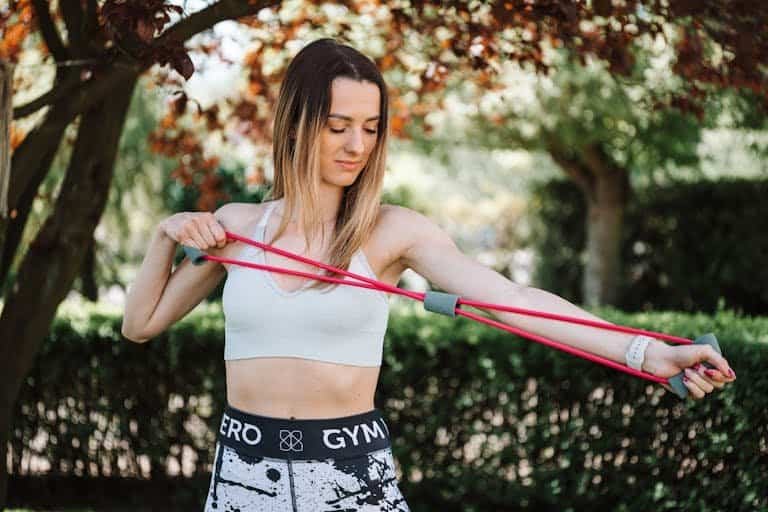 Fit woman using a resistance band for exercise in a sunny outdoor setting.