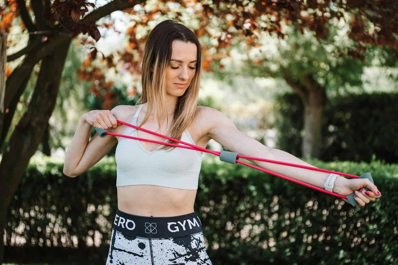 Fit woman using a resistance band for exercise in a sunny outdoor setting.