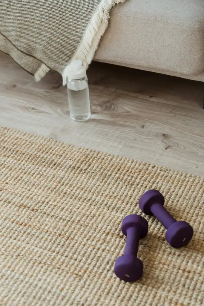 Hex dumbbells and water bottle on jute rug showing minimal home gym equipment for a bedroom