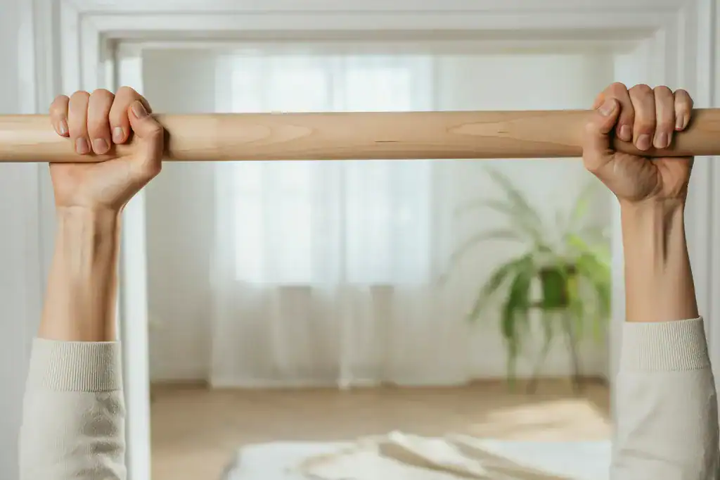 Person holding a wooden bar during yoga practice in a bright room.