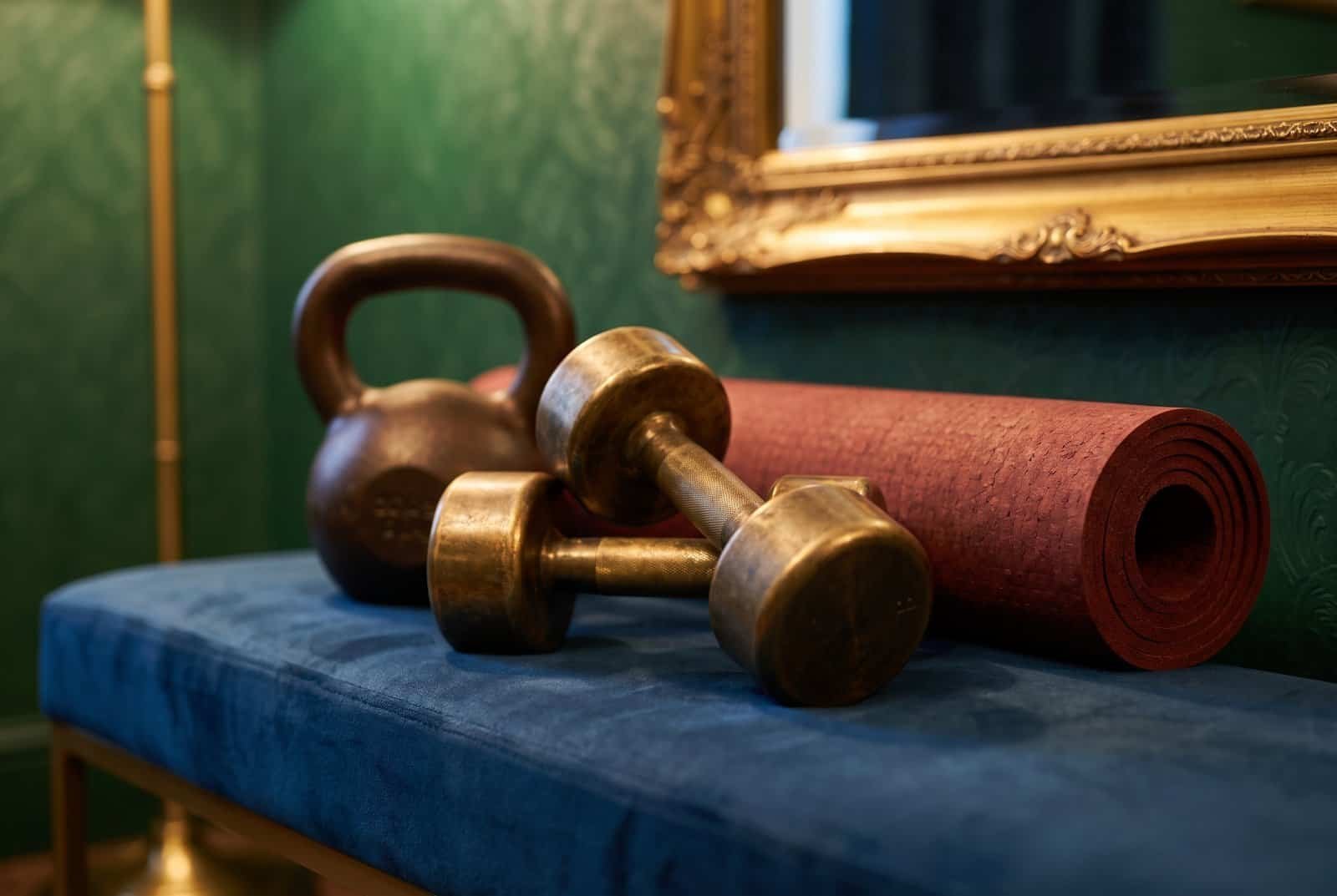 Victorian home gym design detail with brass dumbbells and a bronze kettlebell on a velvet bench